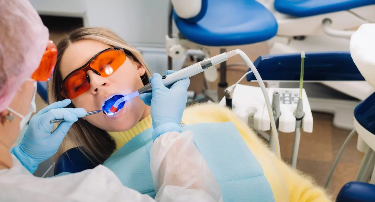 A young beautiful girl in dental glasses treats her teeth at the dentist with ultraviolet light