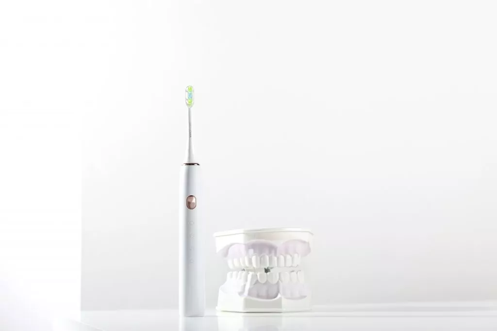 Electronic toothbrush next to jaw model with teeth on light background of bathroom. Minimalism