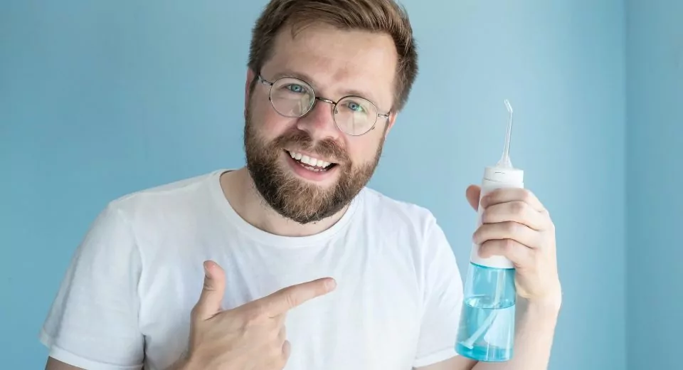 man holds portable irrigator, recommends this oral hygiene product and points to it with finger