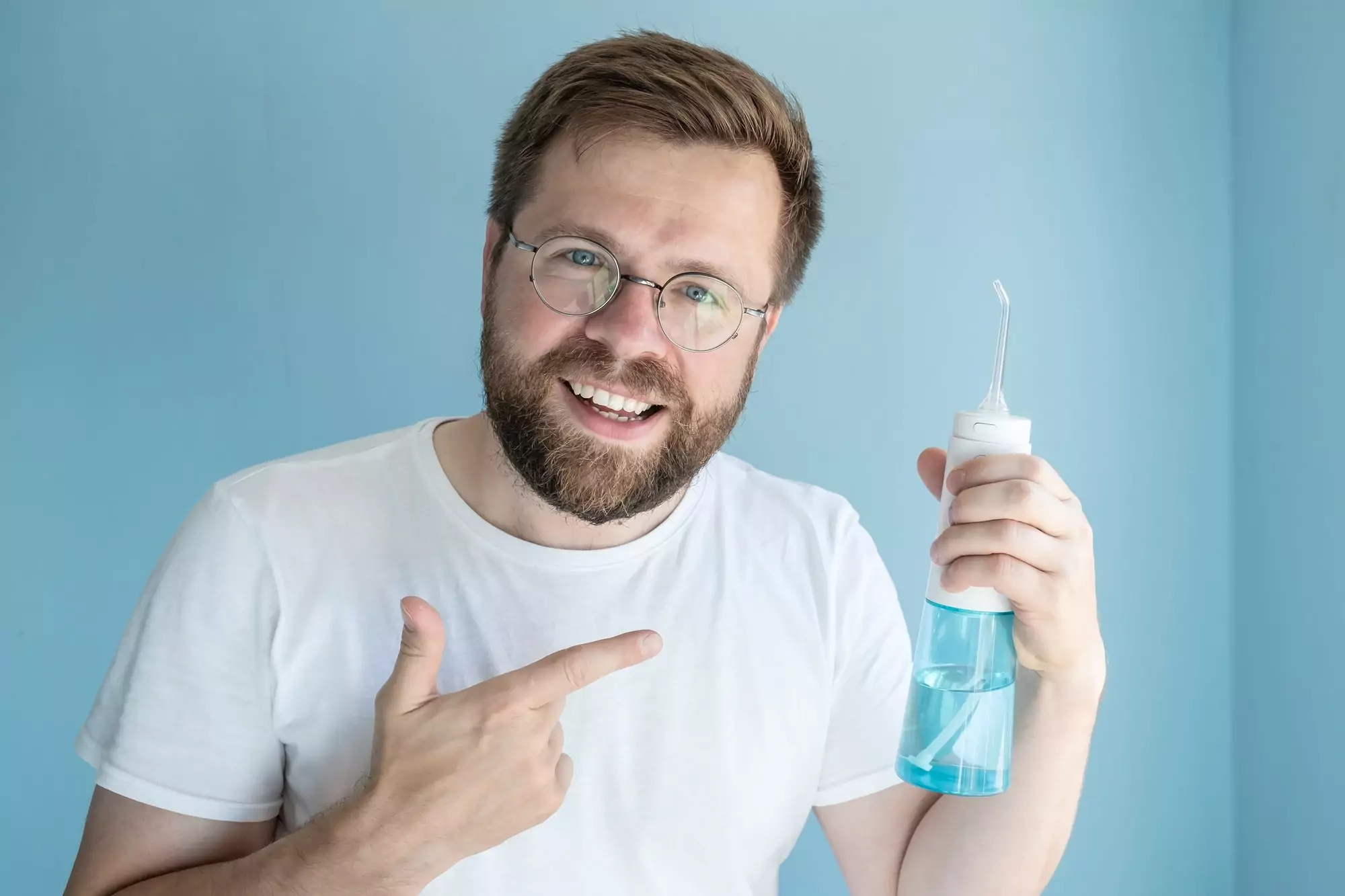 man holds portable irrigator, recommends this oral hygiene product and points to it with finger