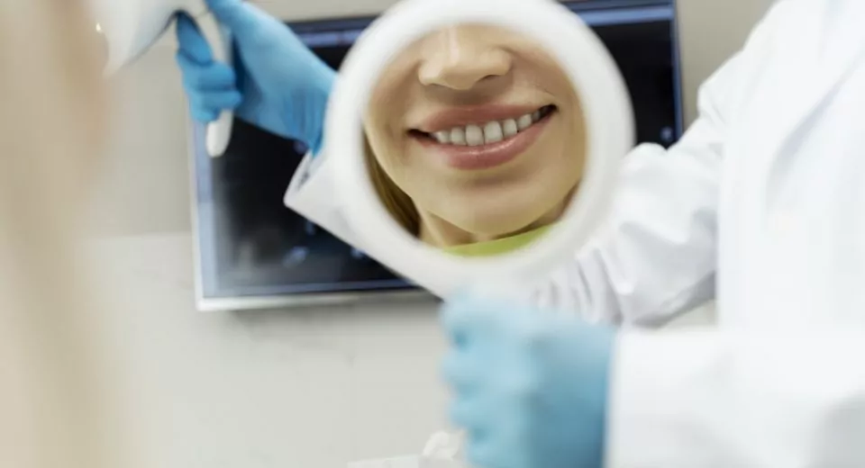 Portrait of female patient with toothy smile looking in mirror after dental treatment. Dental care