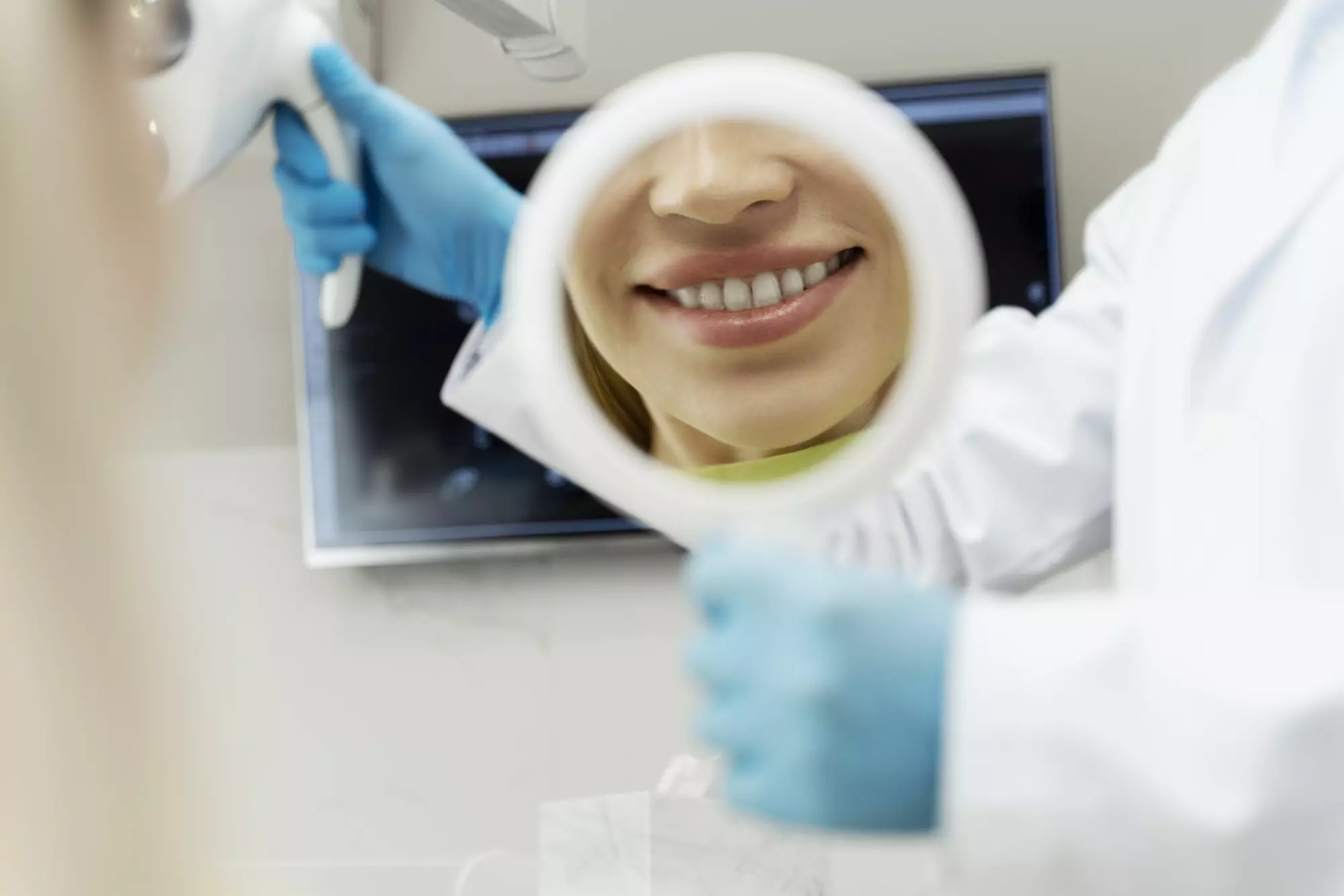 Portrait of female patient with toothy smile looking in mirror after dental treatment. Dental care